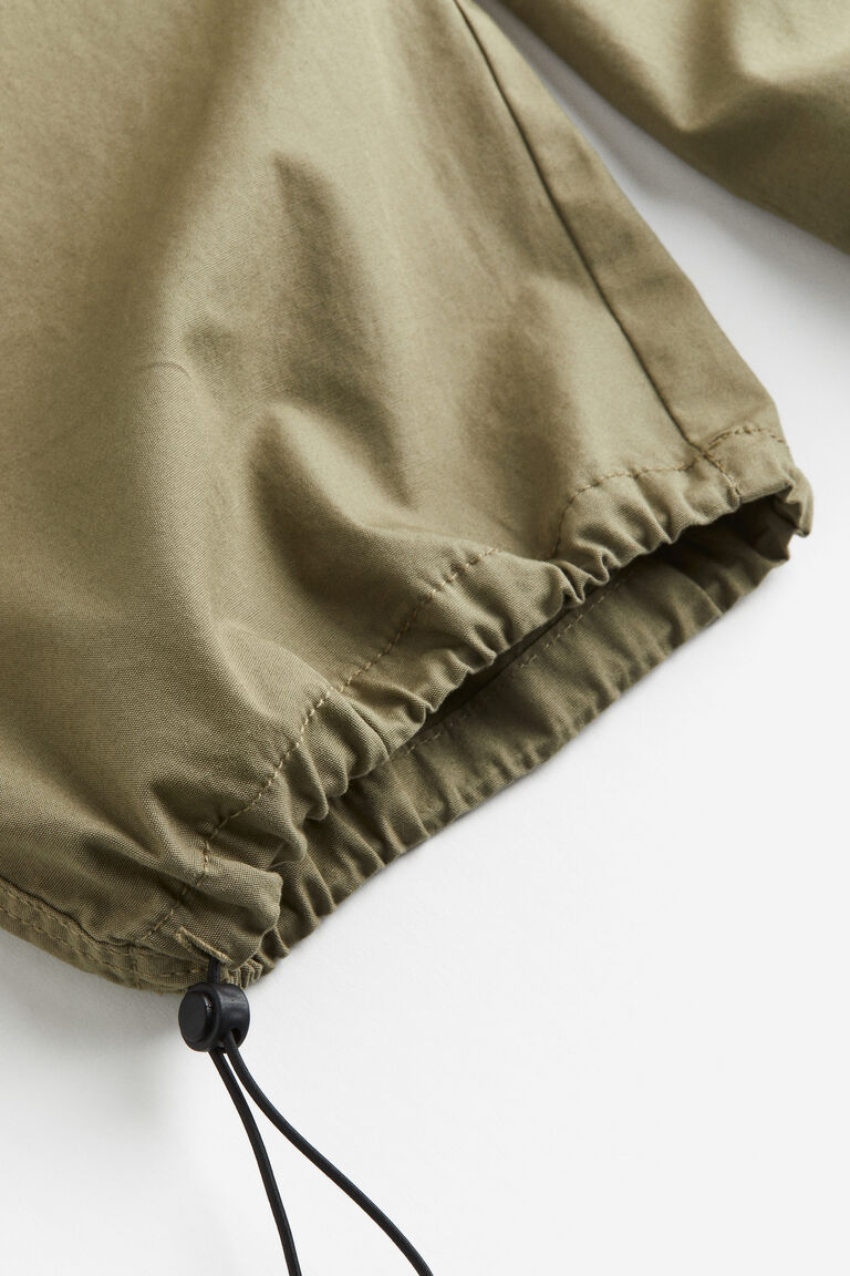 Close-up of an olive parachute pant hem with gathered casing and black cord stopper